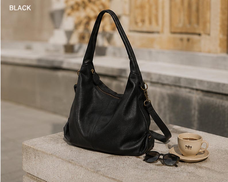 May include: A black hobo-style shoulder bag with a textured surface, a single top handle, and a detachable shoulder strap attached with gold-tone metal hardware. The bag features a zippered main compartment and a slouchy, unstructured silhouette.