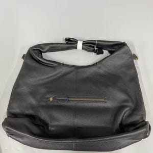 May include: A black hobo-style shoulder bag with a textured surface, featuring a single wide strap, a horizontal zippered pocket on the front with a matching black pull tab, and a small white tag attached to the top handle hardware.