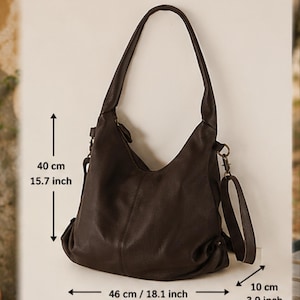 May include: A dark brown hobo bag with a slouchy silhouette, featuring a single shoulder strap and a detachable crossbody strap. The bag measures 15.7 inches in height, 18.1 inches in width, and 3.9 inches in depth, as indicated by the text.