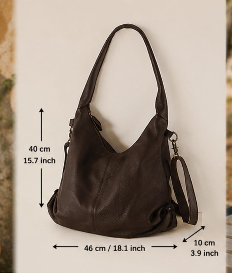 May include: A dark brown hobo bag with a slouchy silhouette, featuring a single shoulder strap and a detachable crossbody strap. The bag measures 15.7 inches in height, 18.1 inches in width, and 3.9 inches in depth, as indicated by the text.