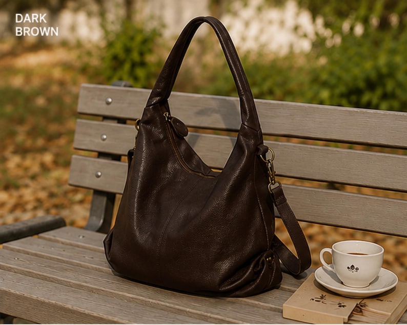 May include: A dark brown hobo bag with a slouchy silhouette, a single top handle, and a detachable shoulder strap with brass-toned hardware. The bag features a zippered top closure and a textured surface. The text "DARK BROWN" is visible in the corner.
