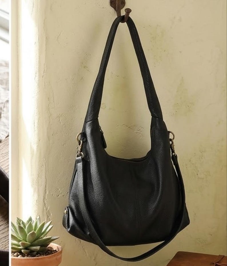 May include: A black hobo-style shoulder bag with a textured surface, featuring a single wide top handle and a detachable crossbody strap attached with brass-toned metal hardware. The bag has a slouchy, rounded silhouette and a zippered main closure.
