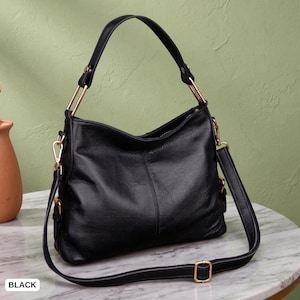 May include: A black hobo-style handbag featuring a textured surface, a single top handle, and a detachable, adjustable shoulder strap. The bag is accented with gold-toned metal hardware, including rectangular handle connectors and strap buckles.