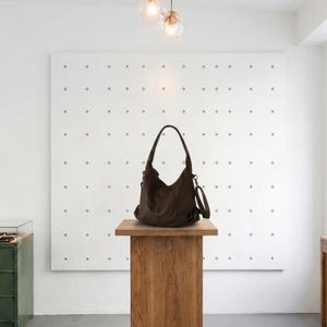 May include: A dark brown hobo-style shoulder bag with a slouchy silhouette, featuring a single top handle, a side strap attachment, and visible stitching details. The bag is constructed with a soft, flexible material and has a spacious main compartment.