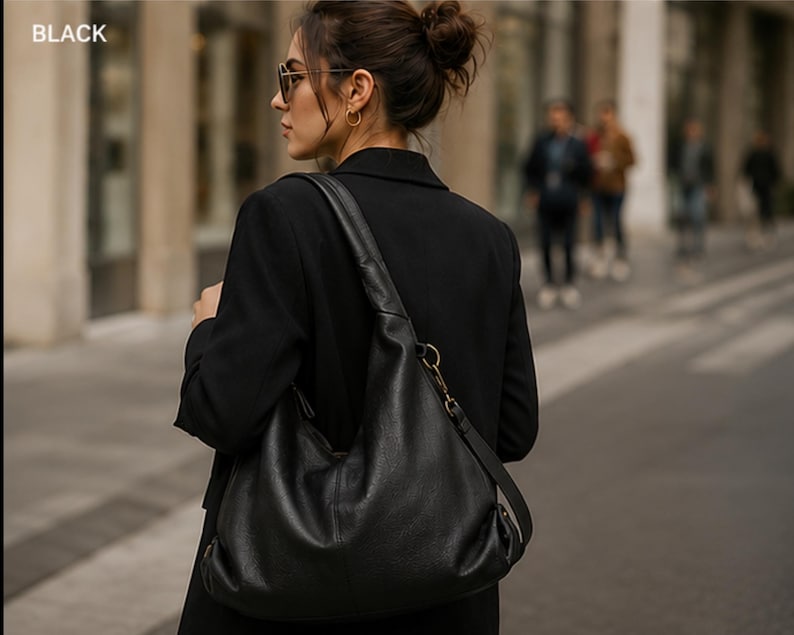 May include: A black hobo-style shoulder bag with a smooth texture, featuring a wide strap, a metallic ring attachment, and a zipper closure. The word BLACK is printed in the upper left corner of the image, indicating the color of the bag.