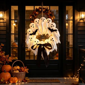 May include: A circular Halloween wreath featuring multiple white ghost figures with black eyes and mouths, accented by black bat silhouettes and a large black ribbon bow, suspended against a dark door frame with warm lighting.