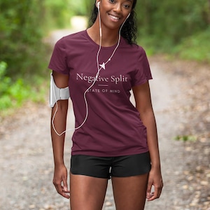 Puede incluir: Una camiseta de manga corta color granate con el texto blanco "Negative Split" sobre el texto más pequeño "STATE OF MIND" y un pequeño gráfico de una zapatilla de correr. La camiseta se combina con pantalones cortos deportivos negros y un brazalete blanco.