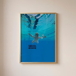 Könnte beinhalten: Ein gerahmter Kunstdruck mit dem Nirvana Nevermind Albumcover. Das Bild zeigt ein Baby, das unter Wasser auf einen Dollarschein an einem Haken zuschwimmt. Der Text NIRVANA und NEVERMIND ist unten mittig in Schwarz auf dem blauen Wasser gedruckt.