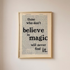 Op de afbeelding: Een ingelijste wandkunstprint met een achtergrond van een vintage woordenboekpagina met de zwarte tekst "those who don't believe in magic will never find it." gedrukt over kolommen van kleine, dichte schreefletters in een gouden lijst.