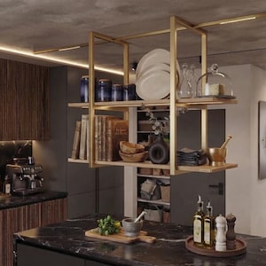 May include: A two-tiered hanging shelf with a gold metal frame and wooden shelves suspended from the ceiling. The shelves hold various kitchen items including white plates, glass jars, books, wooden bowls, a dark vase, and a gold mortar and pestle.