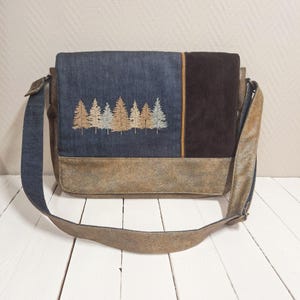 Può includere: Una borsa a tracolla con chiusura a patta, con una foresta di alberi ricamati. La borsa combina denim, velluto a coste marrone e materiali simili alla pelle invecchiata. Ha una tracolla regolabile.
