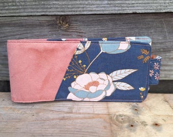 Porta-cheques horizontal feminino, com compartimento para talão de cheques à esquerda, em camurça rosa-claro e tecido floral cinza, com fecho de aba, chique e elegante.