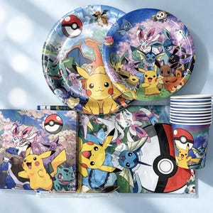 May include: A set of party supplies featuring Pokémon characters including Pikachu, Eevee, and various evolutions. The collection includes two round paper plates, a stack of paper cups, and a pack of napkins, all decorated with colourful graphics.