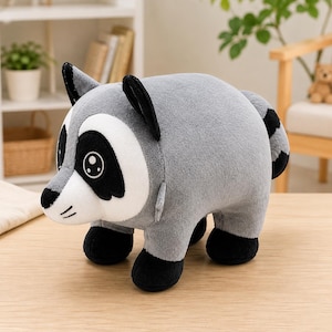 May include: A plush raccoon toy featuring a soft grey body, a white face mask, black eye patches, black ears, and black paws. The raccoon has a striped tail and large, round eyes with white highlights, designed in a rounded, compact shape.
