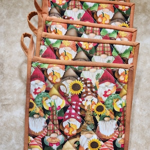 May include: Set of seven brown quilted oven gloves with a gnome and pumpkin pattern. The oven gloves have a brown trim and are quilted with a diamond pattern.