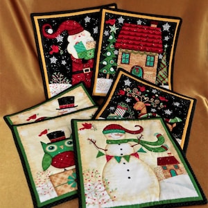 May include: Five Christmas-themed quilted squares with black and green borders. The squares feature a snowman, an owl, Santa Claus, a house, and a reindeer.