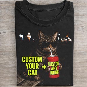 May include: A black t-shirt featuring a graphic of a brown tabby cat wearing black sunglasses and holding a red soda can with a straw. The text on the shirt reads CUSTOM YOUR CAT + CUSTOM ANY DRINK in bright yellow capital letters against a dark background.