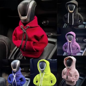 May include: A collection of miniature fabric hoodies designed to cover a car gear shift knob. The hoodies feature a hood, long sleeves, a front pouch pocket, and adjustable drawstrings. Available in red, black, purple, blue, neon yellow, and pink.