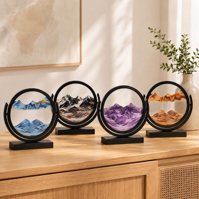 May include: Four circular sand art displays with black frames and rectangular bases. Each piece contains colored sand forming mountain landscapes in blue, black and white, purple, and orange tones, encased between two clear glass panes.