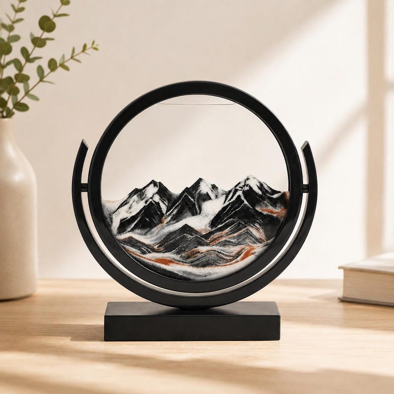Black and white 3D moving sand art forming mountain scenery, modern round glass frame tabletop decor.