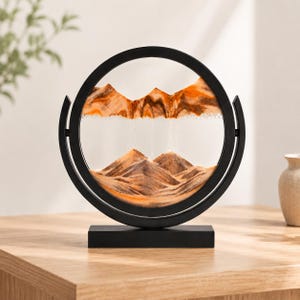 Orange and amber 3D moving sand art showing desert mountain landscape, warm-toned tabletop decor.