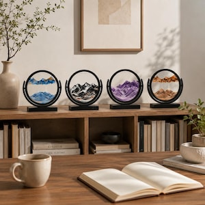 Collection of four 3D moving sand art pieces in blue, black, purple, and orange, displayed on a wooden bookshelf.