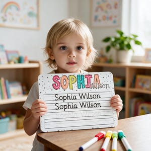 Puede incluir: Una pizarra blanca rectangular para practicar con el nombre SOPHIA en letras coloridas y punteadas, y el nombre Wilson en negro. Debajo, el nombre Sophia Wilson está impreso dos veces en negro y una vez en una fuente punteada gris claro.