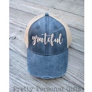 May include: A blue and beige trucker hat with the word "grateful" embroidered in gold on the front.