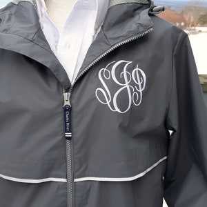 May include: A gray hooded jacket with a white zipper and a white monogram on the front. The jacket has a white reflective strip around the hood and the bottom of the jacket. The zipper pull has the text "Charles River" on it.