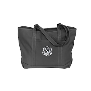 May include: A dark gray canvas tote bag featuring two sturdy shoulder straps and a reinforced bottom panel. The front of the bag displays a white embroidered circular monogram with the letters S, S, and C intertwined in a decorative script font.