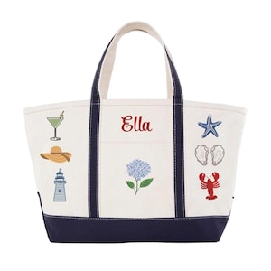 May include: A cream-colored canvas tote bag with navy blue trim and handles. The bag features the embroidered name Ella in red, alongside colorful embroidered icons including a martini glass, sun hat, lighthouse, hydrangea, starfish, oysters, and lobster.