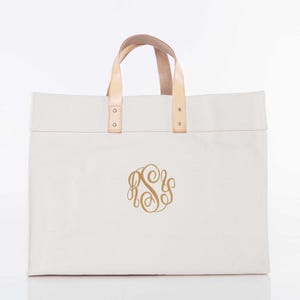 May include: A rectangular off-white canvas tote bag featuring two light tan leather handles secured with silver-toned metal rivets. The center of the bag displays a gold-colored monogram consisting of the intertwined letters R, S, and S in a script font.