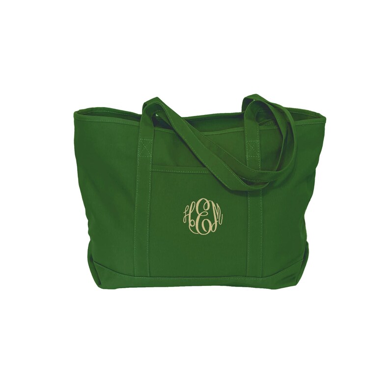May include: A forest green canvas tote bag featuring two sturdy shoulder straps and an exterior slip pocket. The center of the bag is embroidered with a decorative monogram featuring the letters E, H, and M in a light beige thread color.