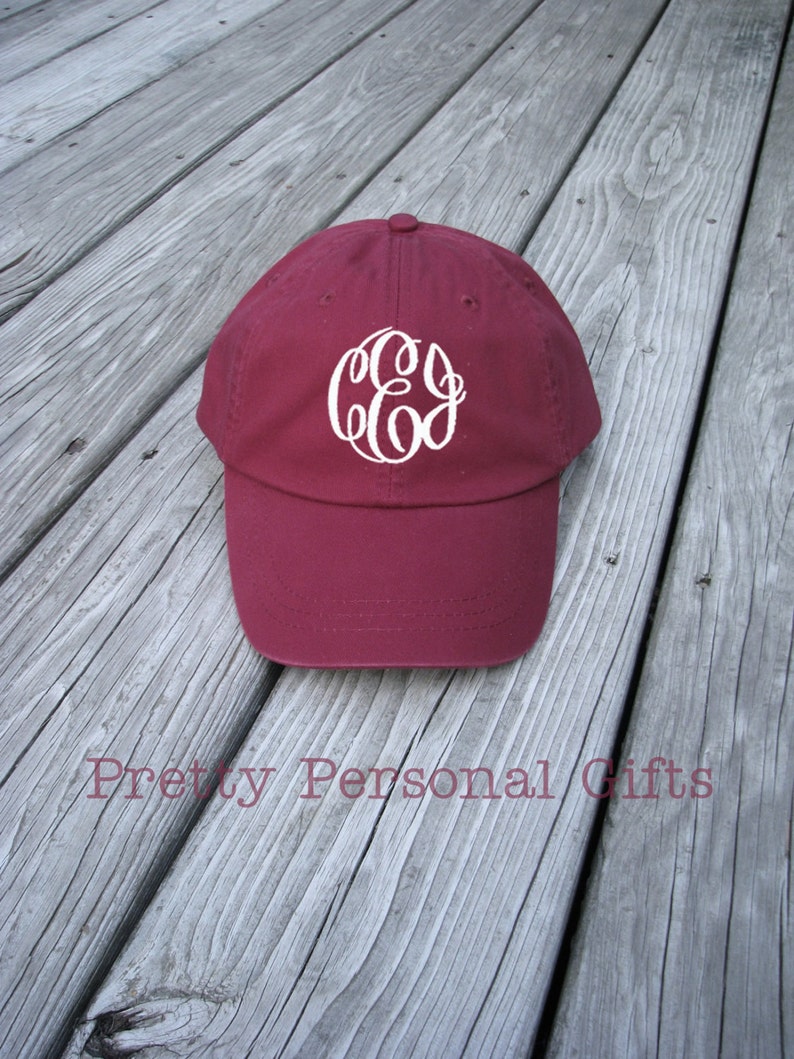 May include: A maroon baseball cap with a white monogram. The cap has a curved brim and a button on top. The text "Pretty Personal Gifts" is printed on the surface.