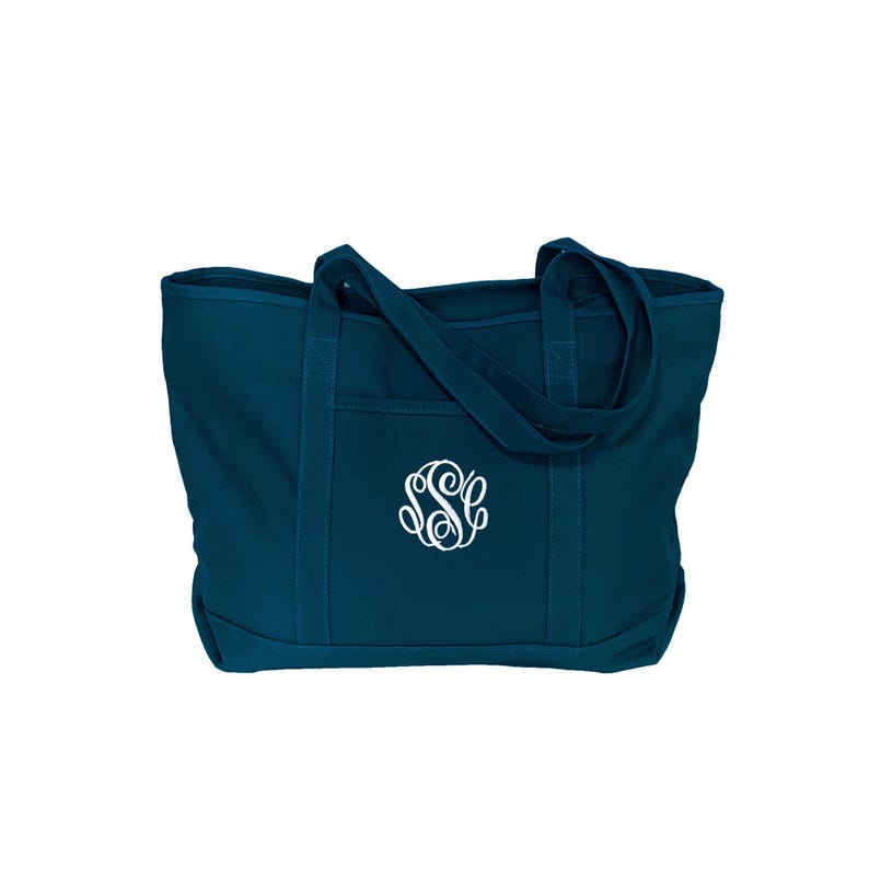May include: A dark teal canvas tote bag featuring two sturdy shoulder straps and an open exterior pocket. The center of the bag is embroidered with a white, decorative, three-letter script monogram featuring the letters S, S, and C.