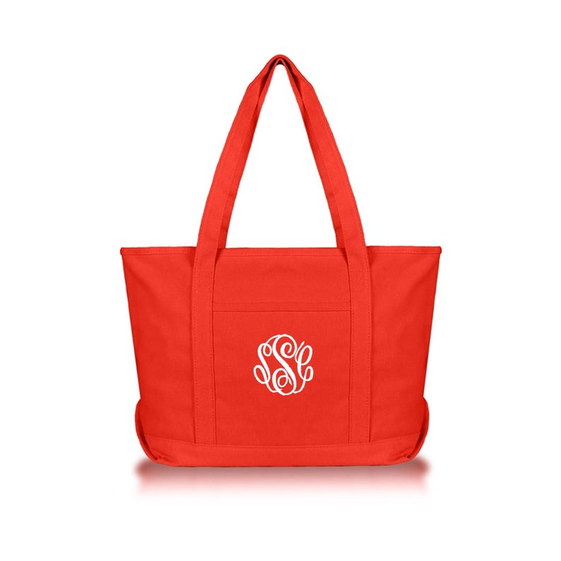 May include: A bright red canvas tote bag featuring two long shoulder straps and a centered white embroidered monogram with the letters S, S, and C in a decorative script font. The bag has a rectangular body with a flat base and vertical stitching.