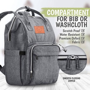 K&ouml;nnte beinhalten: Grauer Wickeltasche-Rucksack mit einem Rei&szlig;verschlussfach mit der Aufschrift "COMPARTMENT FOR BIB OR WASHCLOTH". Die Tasche hat ein Rei&szlig;verschlussfach vorne und ein gro&szlig;es Fach an der Seite. Die Tasche ist aus wasserabweisendem, kratzfestem Stoff.