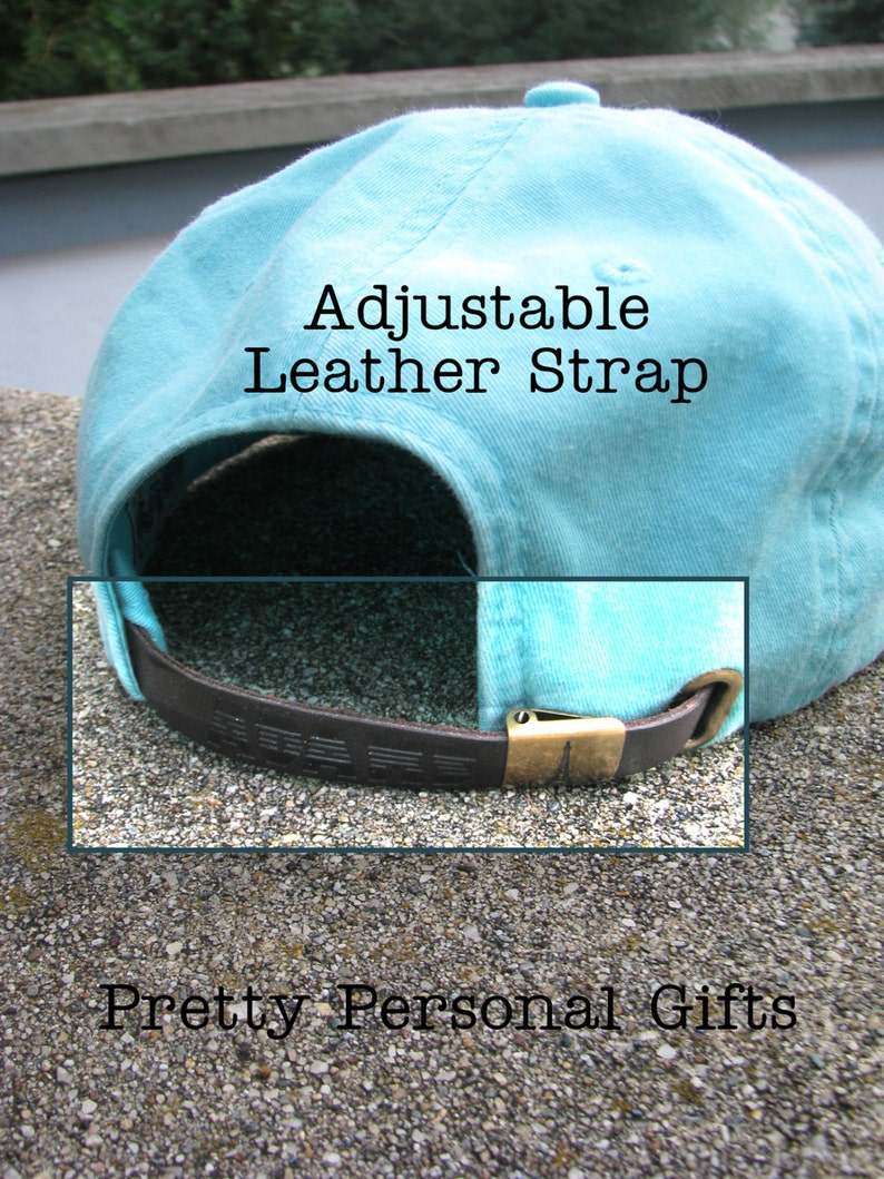 May include: A light blue baseball cap with an adjustable brown leather strap and a brass buckle. The text "Adjustable Leather Strap" is visible on the cap. The words "Pretty Personal Gifts" are also visible.