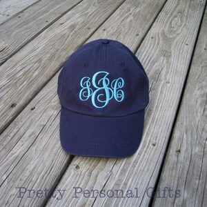 May include: Navy blue baseball cap with a light blue monogram. The cap is sitting on a weathered wooden surface. The text "Pretty Personal Gifts" is visible at the bottom of the image.
