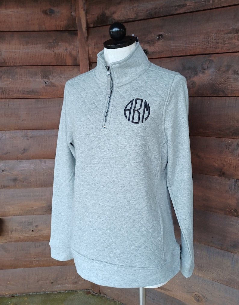 May include: A gray quilted quarter-zip pullover with a black monogram "ABM" on the chest.
