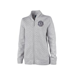 May include: A light gray quilted zip-up jacket with a stand-up collar and a navy blue monogram on the left chest. The jacket has a full-length zipper and ribbed cuffs and hem. The jacket is made of a soft, comfortable material.