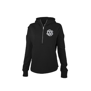 May include: Black hooded sweatshirt with a quarter-zip closure and a white monogram on the chest. The sweatshirt has long sleeves and a kangaroo pocket. The fabric appears to be a soft, comfortable material.