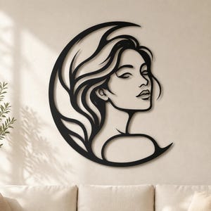 May include: A black metal wall art piece featuring a stylized silhouette of a person with flowing hair integrated into a crescent moon shape. The design uses clean, continuous lines to define the facial features and hair, creating a flat, cutout aesthetic.
