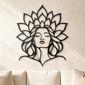 Puede incluir: Una pieza de arte mural de metal negro que presenta la silueta estilizada de una persona con los ojos cerrados, enmarcada por un gran arreglo simétrico de formas de pétalos que crean una estructura similar a una corona sobre la cabeza.