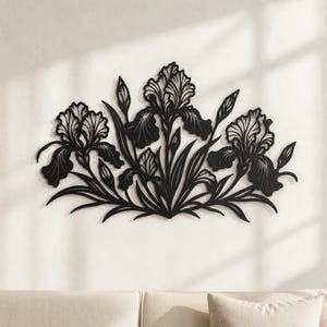 May include: A black metal wall art piece featuring a detailed cutout design of three blooming iris flowers with long, slender leaves and stems. The floral arrangement is symmetrical, showcasing intricate petal textures and pointed buds.
