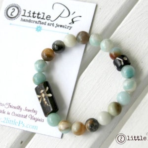 May include: A light blue and brown beaded bracelet with a dragonfly charm. The bracelet is handmade in Coastal Virginia. The text "2 little P's handcrafted art jewelry" and "www.2littlePs.com" is on a white card behind the bracelet.