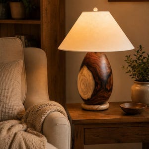May include: A table lamp featuring a smooth, egg-shaped base crafted from dark brown wood with a prominent, lighter-colored natural wood grain knot on the front. The lamp is topped with a wide, off-white conical fabric shade and a small finial.
