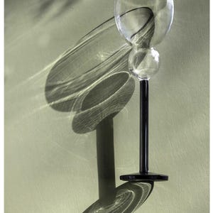 May include: A clear glass goblet featuring a rounded bowl with a small spherical accent on the stem, supported by a solid black stem and a circular black base. The design is characterised by its smooth, transparent glass construction and contrast.