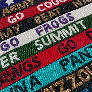 May include: A collection of rectangular beaded straps featuring various team-themed text and symbols. The straps are rendered in diverse colors including red, black, white, green, blue, and gold, with embroidered lettering such as COUGS, FROGS, SUMMIT, DAWGS, PANTHERS, and MIZZOU.