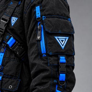 May include: A black jacket featuring bright blue accents, multiple utility pockets, and adjustable straps with plastic buckles. The sleeve displays a triangular patch with a geometric design, and the fabric has a textured, dark finish.
